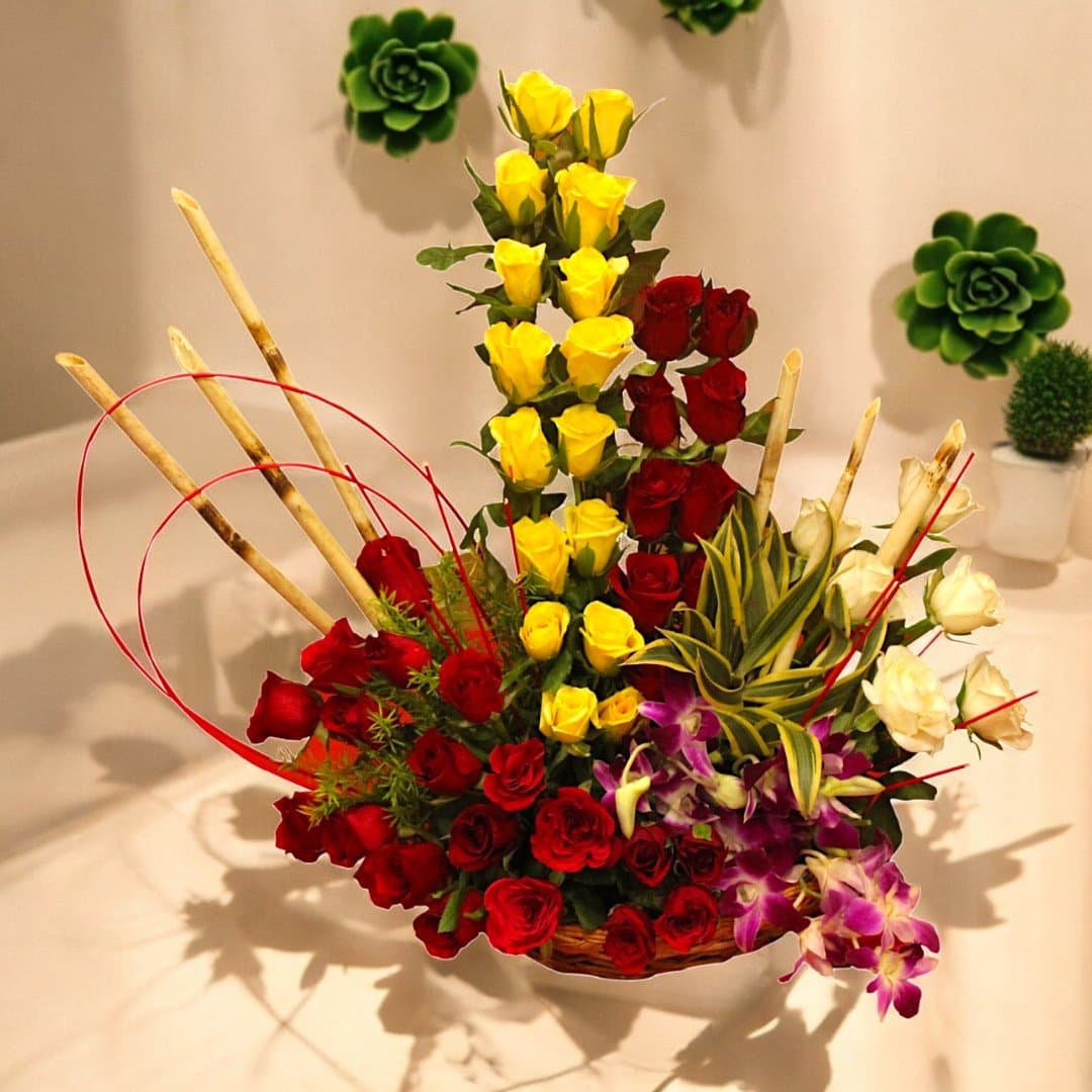 Vibrant floral arrangement with yellow, red, and white roses, and orchids by BetterGiftFlowers.